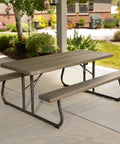 Six Foot Folding Picnic Table With Classic Rugged Steel Frame Seats Eight UV Protected Top Weather And Rust Resistant Flat Fold For Easy Stow And An Umbrella Hole For Backyard Hangouts in a garden setting.
