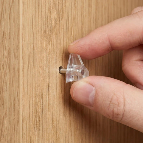 Inserting clear Plastic Shelf Support Pins 3mm with Studs 60 Pack into wooden cabinet, showing easy tool-free install.