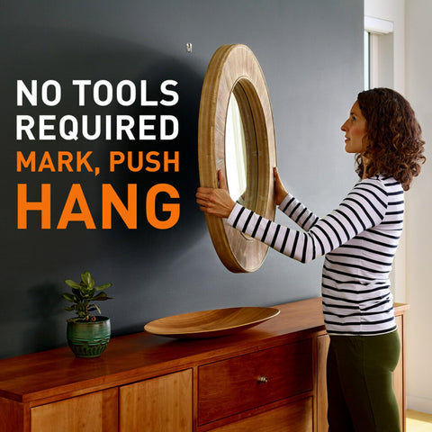 Woman using heavy duty drywall picture hanger that holds up to 65 pounds; installs in seconds with a quick push; no tools required