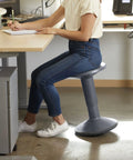 Person seated on SitWell Wobble Stool With Adjustable Height For Active Seating In Classrooms And Libraries, gray finish, office setting.