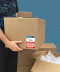 Person holding box with Massive 600 Count Moving Box Labels Pack For Three To Four Bedroom Homes With Writable Note Areas.