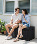 Two people sitting on a 78 Gallon Waterproof Resin Deck Box With Lockable Bench No Fuss Outdoor Storage, black resin rattan pattern.