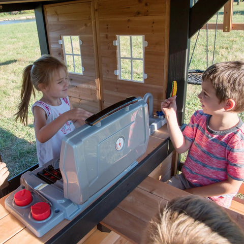 Children playing with kitchen in Cedar Wood Swing Set With Wave Slide And Elevated Clubhouse Play Kitchen And Picnic Area Belt And Web Swings Rock Wall Balconies Playhouse Step Ladder And Outdoor Family Playset For Backyard Fun And Imaginative Outdoor Playtime