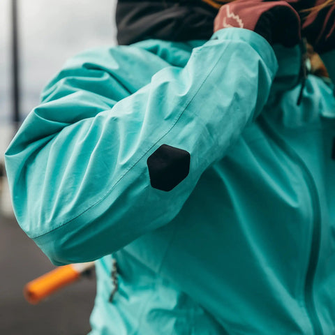 Person wearing jacket with Hex Peel And Stick Repair Patches Kit With Two 2.5 Inch And Two 1.5 Inch Patches In Clear And Black No Sew No Heat Quick Fix For Holes And Burns On Down Jackets Rain Gear Tents Backpacks And Other Outdoor Nylon Gear applied on sleeve