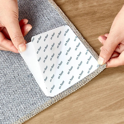 Hands applying anti slip rug grips 12 pack for hardwood floors and wood area rugs white rubber backing rug tape on a rug corner
