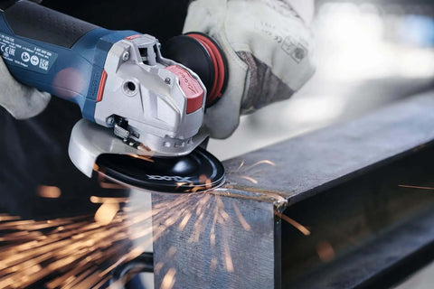 Built Different Five Inch Angle Grinder Crunches Concrete And Metal Up To 11500 RPM Using A Brutal 13 Amp Motor Paired With A Quick Change X Lock System And Ergonomic Paddle Switch For Zero Fatigue, cutting steel with sparks flying.