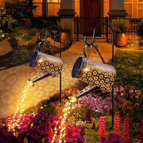 Solar Powered Watering Can Lantern Lights For Garden Decor illuminating a garden pathway at night, hanging from hooks.