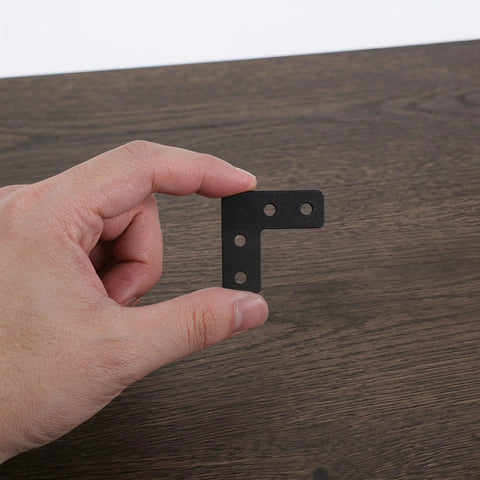 Close-up of hand holding a bracket from 20 Pack Black Stainless Steel Corner Brackets With Enhanced 90 Degree Design For Wall Mounts
