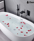 Water running from a wall mounted matte black tub faucet with hand shower into a freestanding tub with rose petals, modern look.