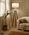 Levi LED Floor Lamp With Tall Black And Gold Tripod For A Dope Living Room Vibe, placed beside a white couch and indoor plant.
