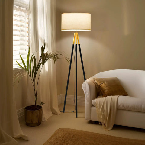 Levi LED Floor Lamp With Tall Black And Gold Tripod For A Dope Living Room Vibe, placed beside a white couch and indoor plant.
