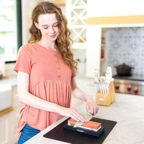 Woman using Pro Grade Knife Sharpening Kit With Whetstone Bowl, 15-Piece Set on kitchen counter with dual grit stones.