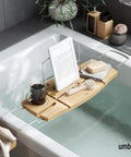 Aquala Extendable Bathtub Tray Caddy With Book Stand And Wine Glass Holder, holding tablet and bath accessories in a spa setting