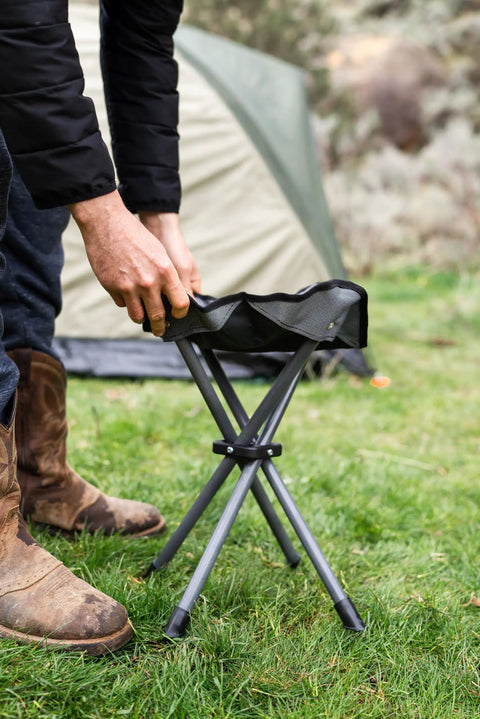 Apex Fold-Up Stool G-140 Black Grey Ultra Portable Camp Seat being set up beside a tent outdoors.