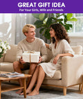 A couple sitting on a sofa with a gift box, surrounded by a vase of flowers and a wooden coffee table, in a cozy living room setting.