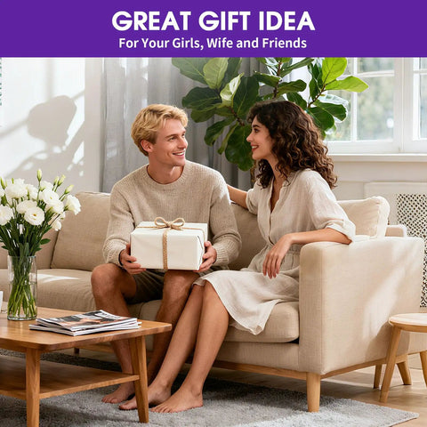A couple sitting on a sofa with a gift box, surrounded by a vase of flowers and a wooden coffee table, in a cozy living room setting.