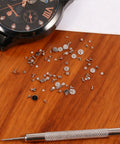 100 Piece Watch Screw Set With Micro Battery Clamp Screws on wooden surface with watch and screwdriver