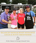 Group of four people holding coffee cups in front of a coffee truck with balanced medium roast banner.