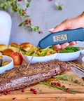 Hand using Instant Read Thermapen Inspired Digital Food Thermometer In Cayenne Red to measure beef temperature on cutting board