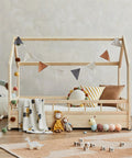 Wooden house-shaped children's bed with decorative pillows, blanket, and toys, including a plush caterpillar and monkey doll.