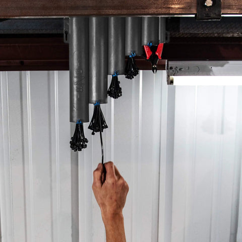 Hand reaching for zip tie on Magnetic Base Cable Tie Organizer With 250 Zip Ties And Cutter mounted in garage