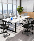Office room with multiple ergonomic gaming chairs with lumbar support and armrests around a conference table, grey mesh back design.
