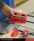 Person using industrial grade heavy duty plug lockout device for lockout tagout in red, OSHA compliant nonconductive polypropylene.