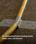 Water droplets on Extra Heavy Duty Olive Duct Tape 6969 sealing a yellow cable on concrete, highlighting water resistance and strength.