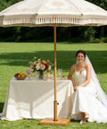 Bride sitting under umbrella shading a table with flowers and desserts, using Beefy 43 Lb Concrete Patio Umbrella Base Teak Brown Square Outdoor Stand.
