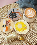 Three completed coasters from the Eight Pack Landscape Diamond Painting Coasters With Holder Complete DIY Kit For Adults Round Full Drill 5D Gem Dots Craft Set With Pen Glue Tray For Home Decor And Party Time displayed with a coffee cup.