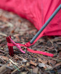 Red Groundhog Tent Stake in soil with guy line attached, showcasing 7.5 inch size and Y-beam design, Reflective Pull Loop visible.