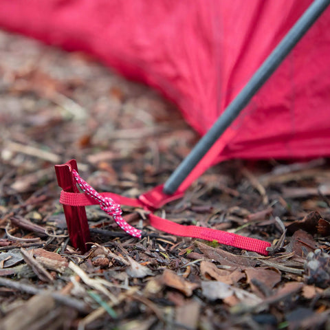 Red Groundhog Tent Stake in soil with guy line attached, showcasing 7.5 inch size and Y-beam design, Reflective Pull Loop visible.