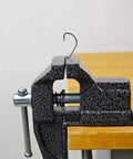 Side view of 2 In 1 Mini Bench Vise And Hook Sharpener For Diyers, clamped to wooden table edge, showing metal jaws and screw mechanism.