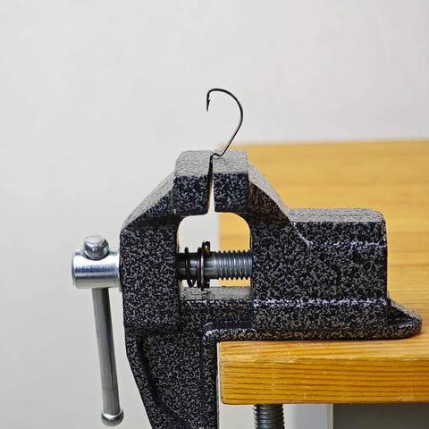 Side view of 2 In 1 Mini Bench Vise And Hook Sharpener For Diyers, clamped to wooden table edge, showing metal jaws and screw mechanism.
