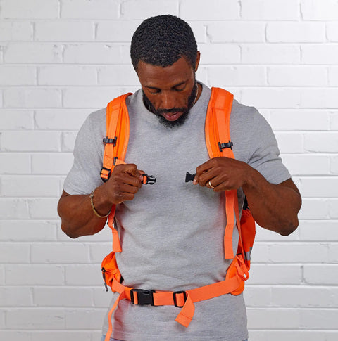 Man adjusting straps on Hi Vis Orange Safety Backpack With Reflective Panels, Adjustable Hard Hat Holder, Bottle Holders, and Hydration Reservoir