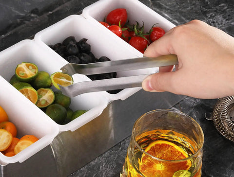 Hand using Restaurant Grade 6.5 Inch Pom Tong Set Of 6 Stainless Steel Garnish Tongs with satin finish to pick lemon slice