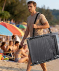 Man carrying Face Hole Tanning Loungers Set Of 2 Folding Outdoor Lounge Chairs with Five Position Recline at a beach.