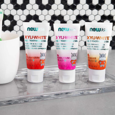 Three tubes of XyliWhite Kids Toothpaste Gel in Strawberry, Bubblegum Splash, and Orange on a bathroom counter.