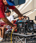 Man using gas powered portable generator with carrying handle 1200W running power and 1200 peak watts black and gray at a campsite.
