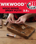 Person using KwikWood Wood Repair Epoxy Putty Stick 1 Oz Beige Tan For Rotted Wood Repairs on a wooden board.