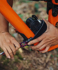 Hands attaching Rockband Bicycle Gear Carrier Strap In Orange No Drop Mount For Inner Tubes And Tools on a bike frame
