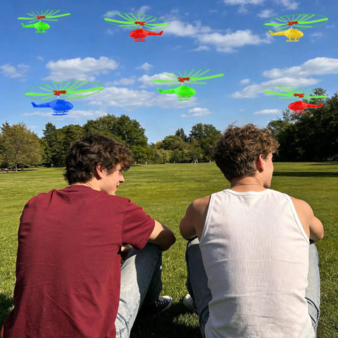 Two people in a park watching colorful helicopters flying, part of the Colorful Helicopters And Airplanes Set With Launcher, 20 Flying Toys.