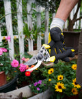 Gardener holding Pro Grade Pruning Shears For Gardening With Non Slip Ergonomic Handles And Blade Cover in a flower garden
