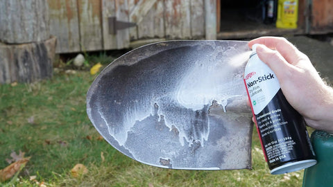 Person applying Dry Film Teflon Non-Stick Lubricant Aerosol, 10 Oz, Ultra-Slick Dirt-Repelling Coating to a metal shovel blade.