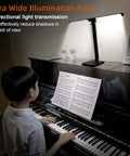 A person playing piano illuminated by a Led Desk Lamp For Home Office With USB Charging Port, Rotatable Aluminum Piano Lamp For Upright Piano, Eye Caring Reading Light In Glossy Black, Desk Setup On Point With Three Dimmable Modes And Easy Brightness Control.
