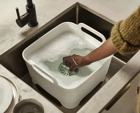 Person using Wash And Drain Kitchen Dish Tub With Handles And Twist Drain Plug 9 Liter Basin For Home RV Or Camping Use.