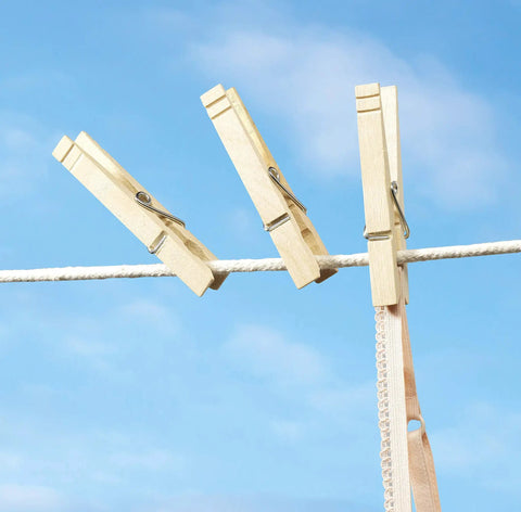 Natural Wood Clothespins 50 Pack Built Different Heavy Duty Wooden Clips With Rust Resistant Springs For Laundry Lines holding fabric outdoors.