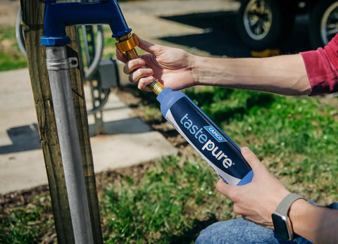 Person connecting TastePure RV Water Filter Inline System With Flexible Hose Protector Six Step Filtration GAC And KDF to outdoor spigot