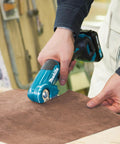 Person using Badass Compact 12V Max Lithium Ion Cordless Multi Cutter to trim flexible material on a work surface.