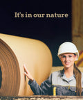 Woman in safety gear touching large roll of paper in manufacturing setting, showcasing industrial work environment.